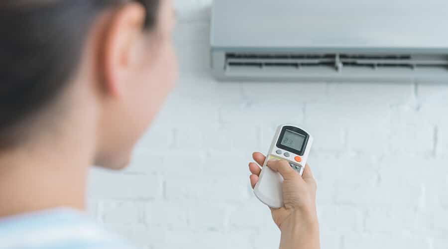 A person pointing a remote control at an AC unit
