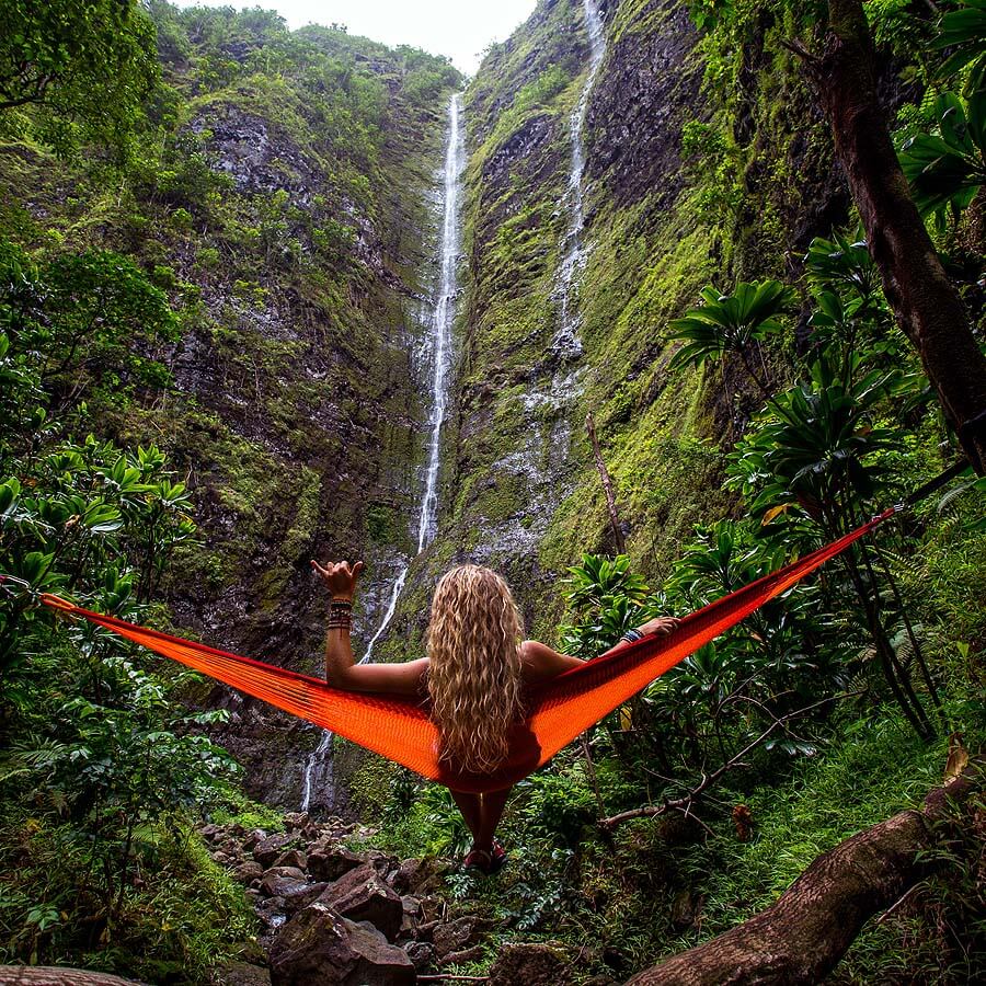 A woman sitting on a hammock by a waterfall
